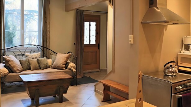 A cozy living room with a sofa, wooden coffee table, and a kitchen area with a stove and microwave. - Villa 'L'autre Vie Là' with Mountain Views, Private Terrace and Wi-Fi (La Bourboule)