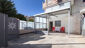 A covered patio area with a table and chairs, a grey gate with a sun symbol, and a building with a balcony. - Apartment 'Casa Luxury' with Shared Terrace, Wi-Fi and Air Conditioning (Santeramo In Colle)