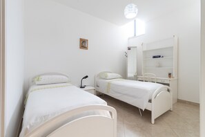 Un dormitorio con dos camas, un escritorio, una silla, un estante pequeño y una ventana.