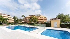 Et poolområde med to pools, en mindre bygning og boliger i baggrunden.