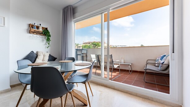 En moderne stue med et glasbord, stole, en sofa og en balkon med udsigt.