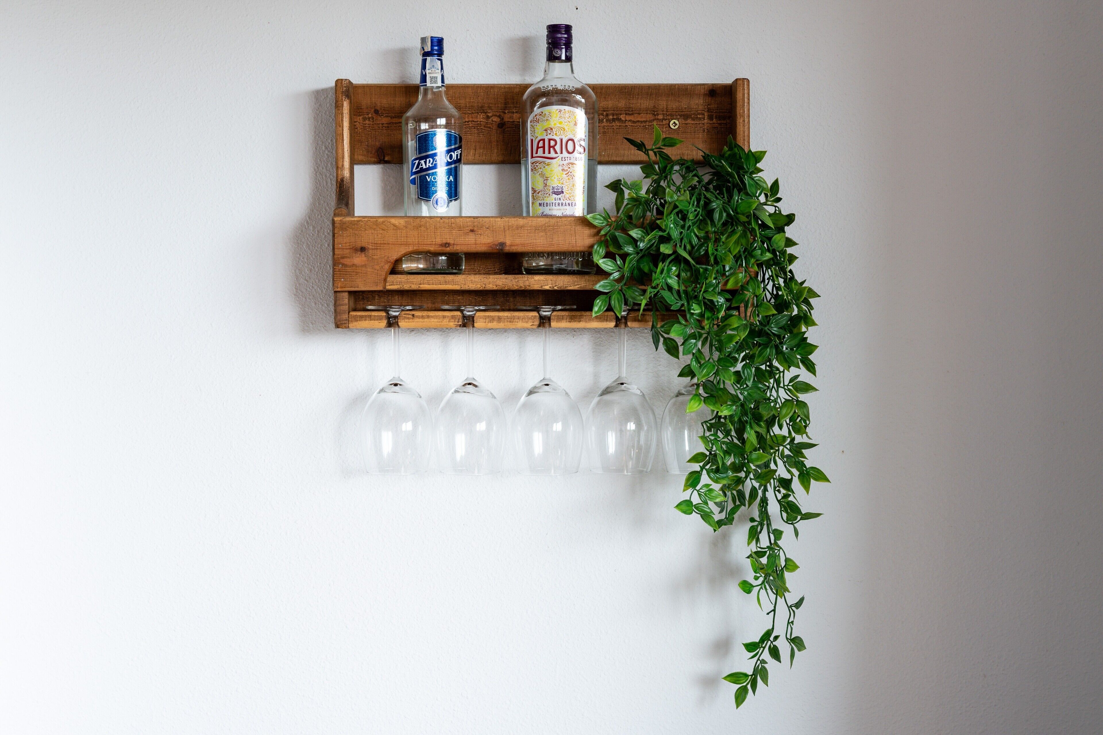 A wooden shelf with two bottles and a plant, and a row of empty wine glasses below.