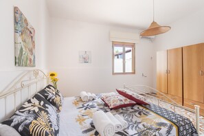 A bedroom with a bed, pillows, a vase with flowers, a window, and a wardrobe.