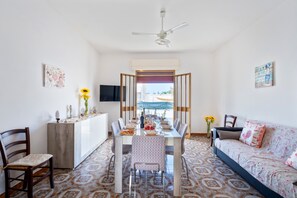 A dining area with a table set for six, chairs, a sofa, a TV, and a ceiling fan.