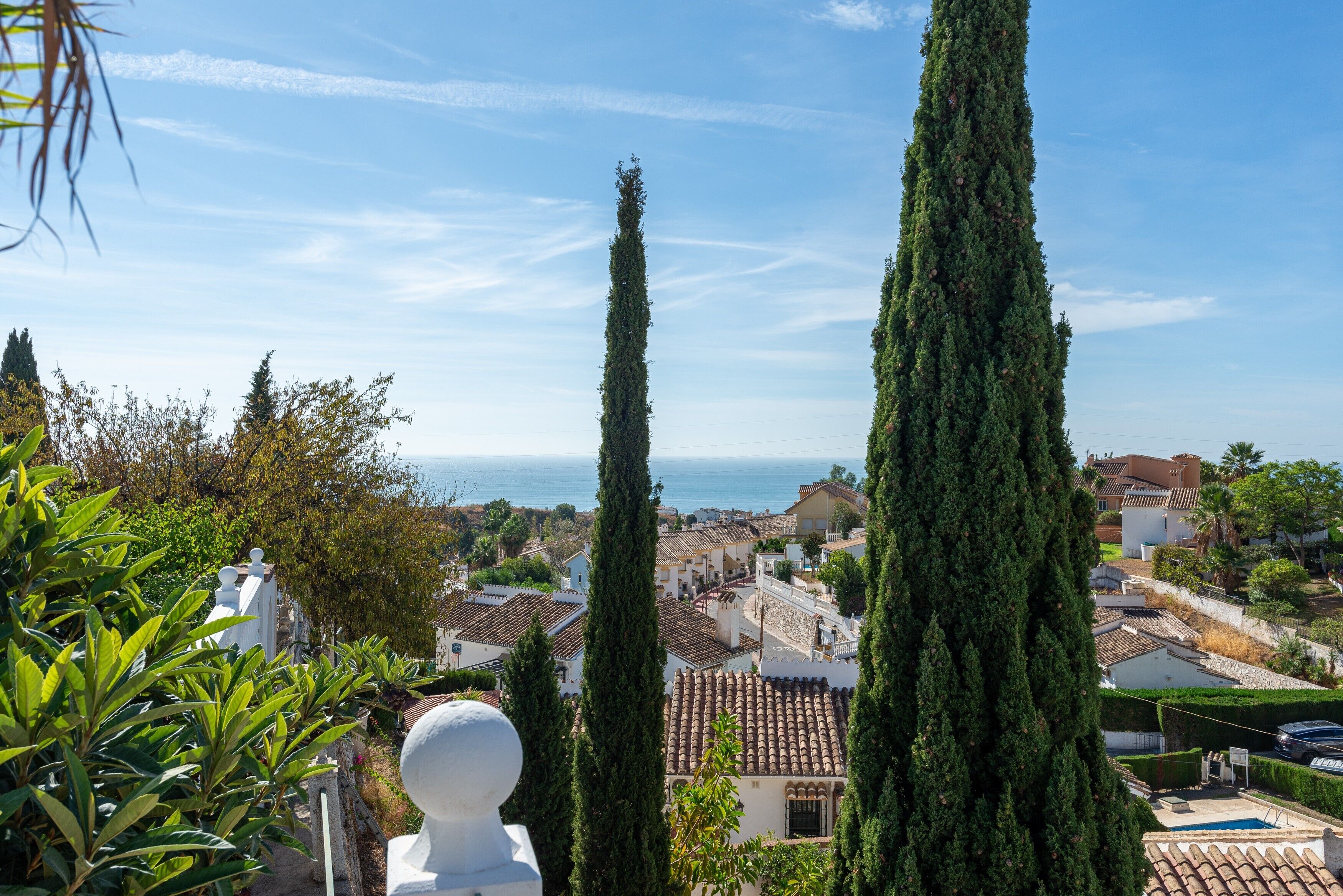 Un pueblo costero con altos cipreses, edificios de tejados de terracota y una vista despejada al mar.