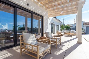 A modern outdoor patio with bamboo furniture, large windows, and a view of the cityscape. - Holiday Home 'Villa with Privat Saltwater Pool' with Sea View, Wi-Fi and Air Conditioning (Benalmádena)