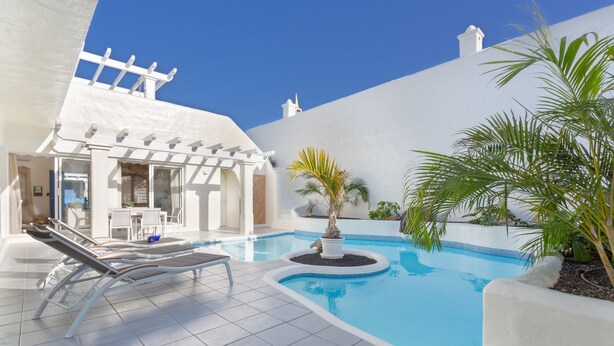 Une piscine avec des chaises longues, une pergola et des plantes en pot.