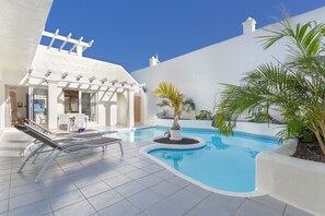 A swimming pool with lounge chairs, a pergola, and potted plants.