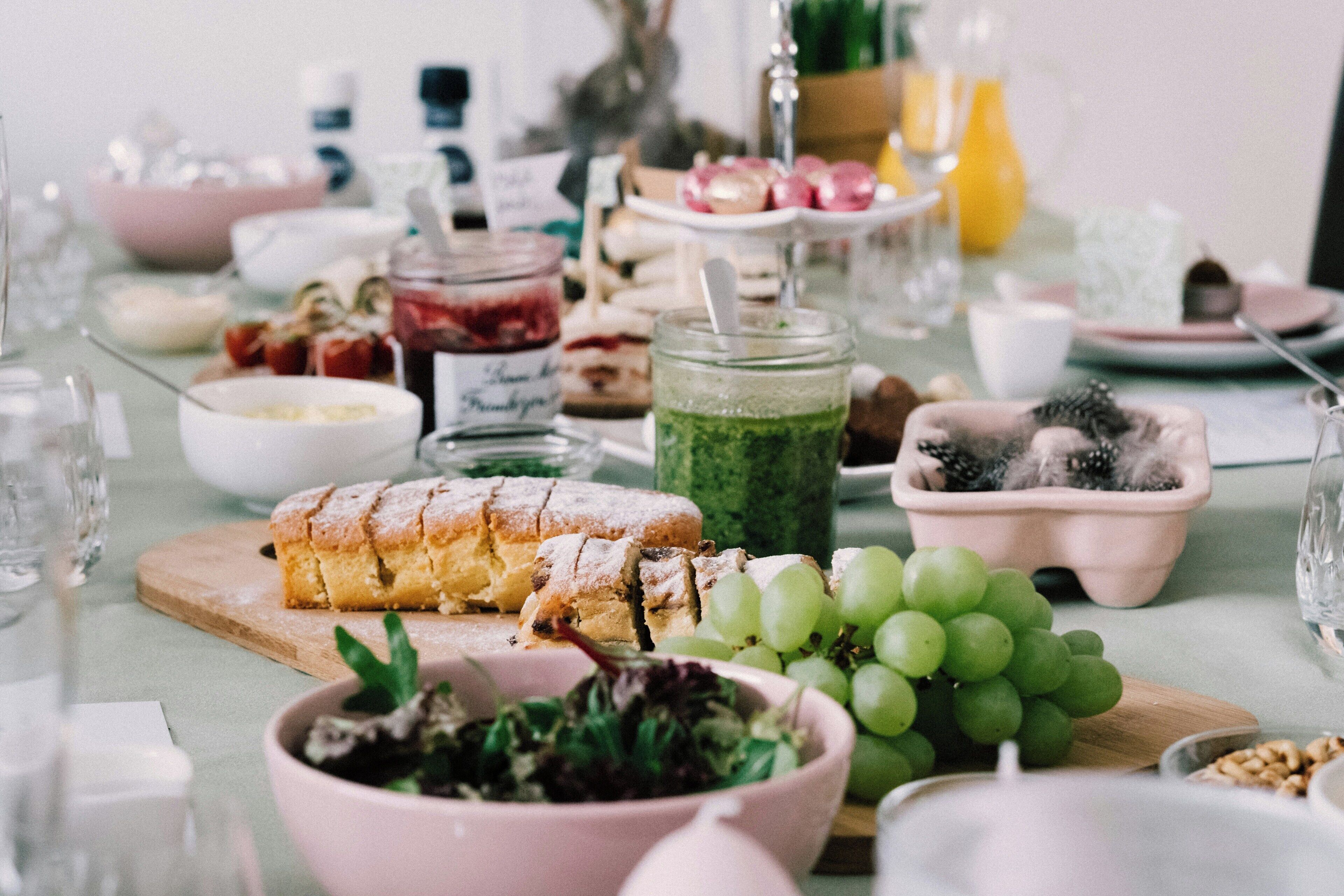 Une table dressée avec divers aliments, notamment une miche de pain, un saladier rempli de salade et une assiette de raisins.