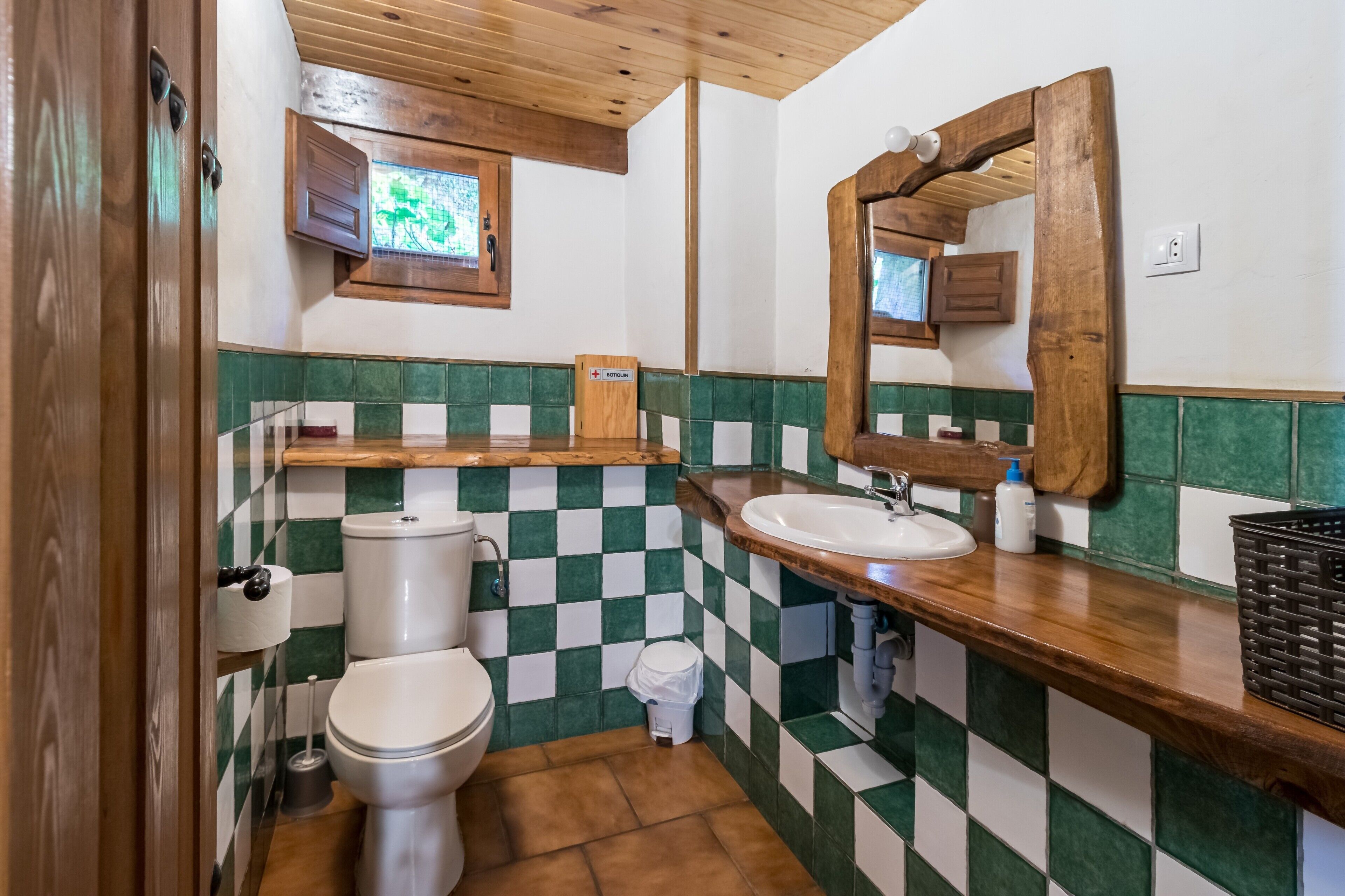 Een badkamer met een betegelde muur in ruitpatroon, een houten wastafelmeubel en een spiegel.