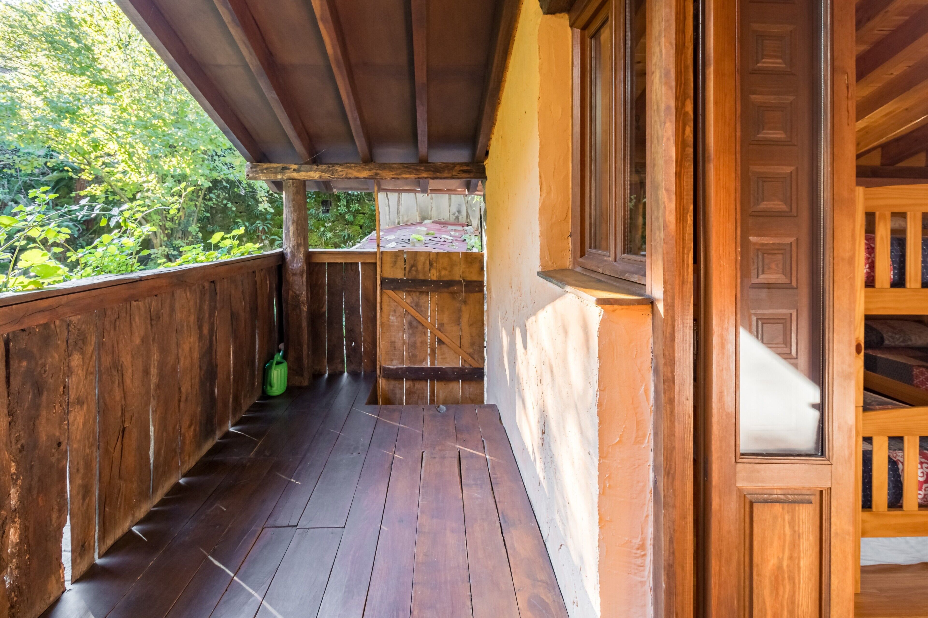 Un balcón de madera con vistas a la vegetación, baranda de madera y una ventana.