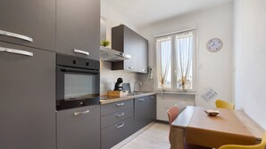 A modern kitchen with grey cabinets, a built-in oven, and a dining area with a wooden table and yellow chairs.