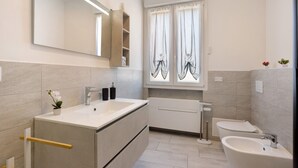 A modern bathroom with a large mirror, two sinks, a bathtub, and a toilet.
