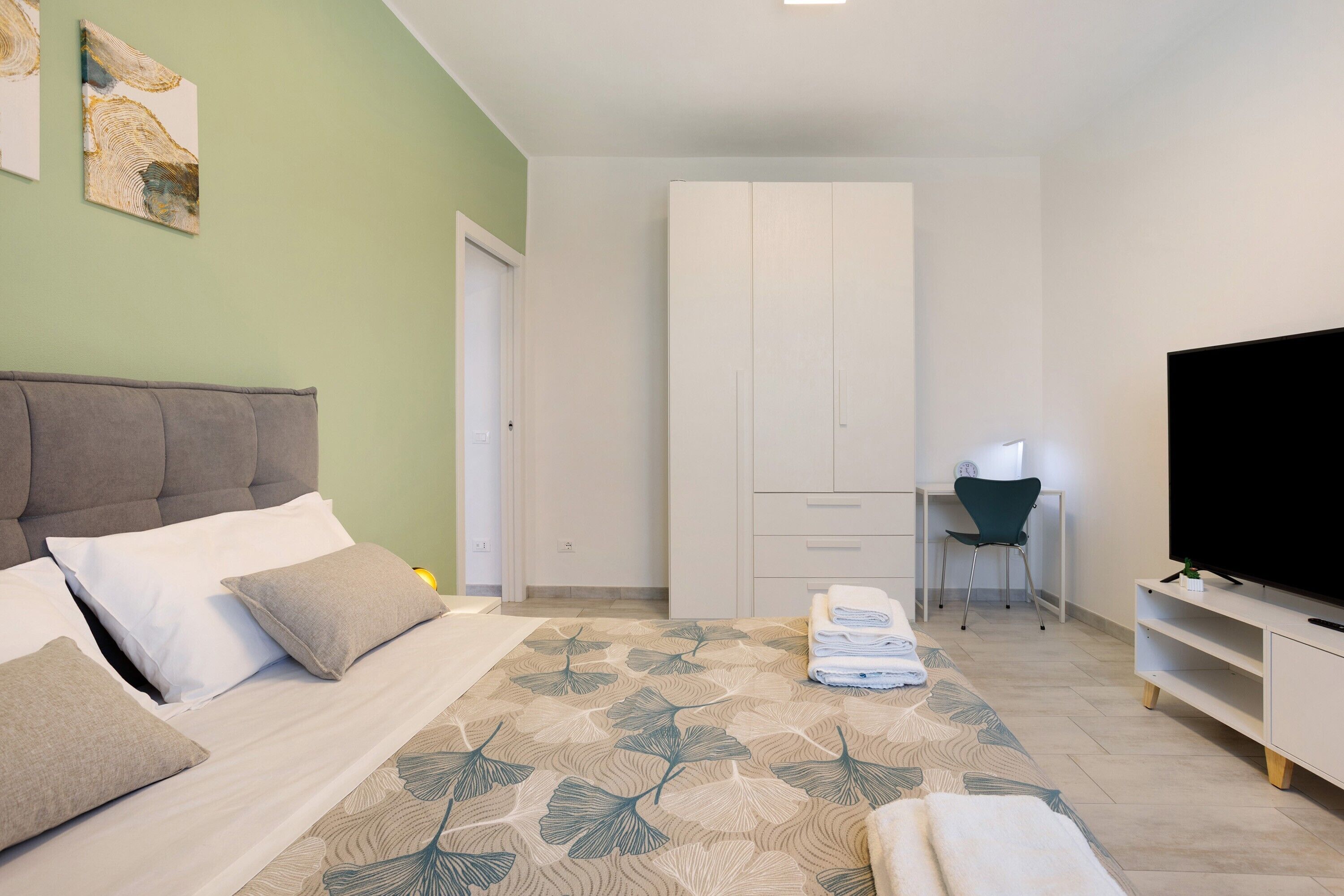 A bedroom with a bed, a desk, a chair, and a TV.
