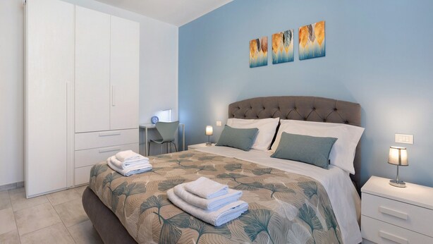 A bedroom with a bed, bedside tables, a desk, and artwork on the wall.