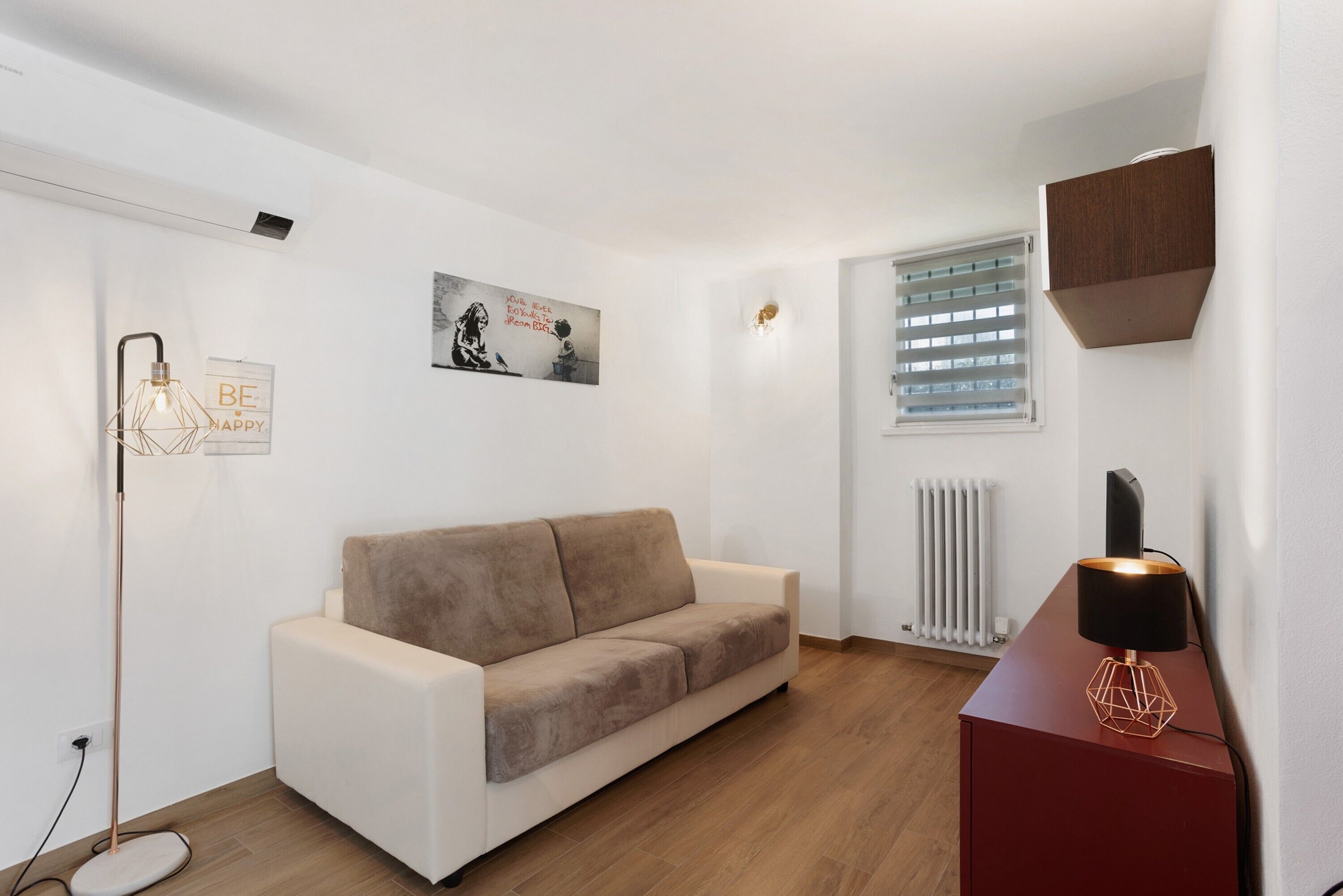 Un salon moderne avec un canapé, une lampe sur pied, un radiateur et un meuble fixé au mur.