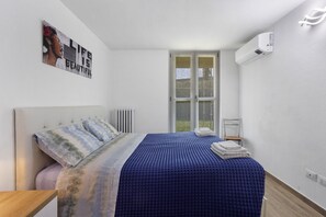 Une chambre à coucher avec un lit, un radiateur, une fenêtre et un appareil de climatisation.