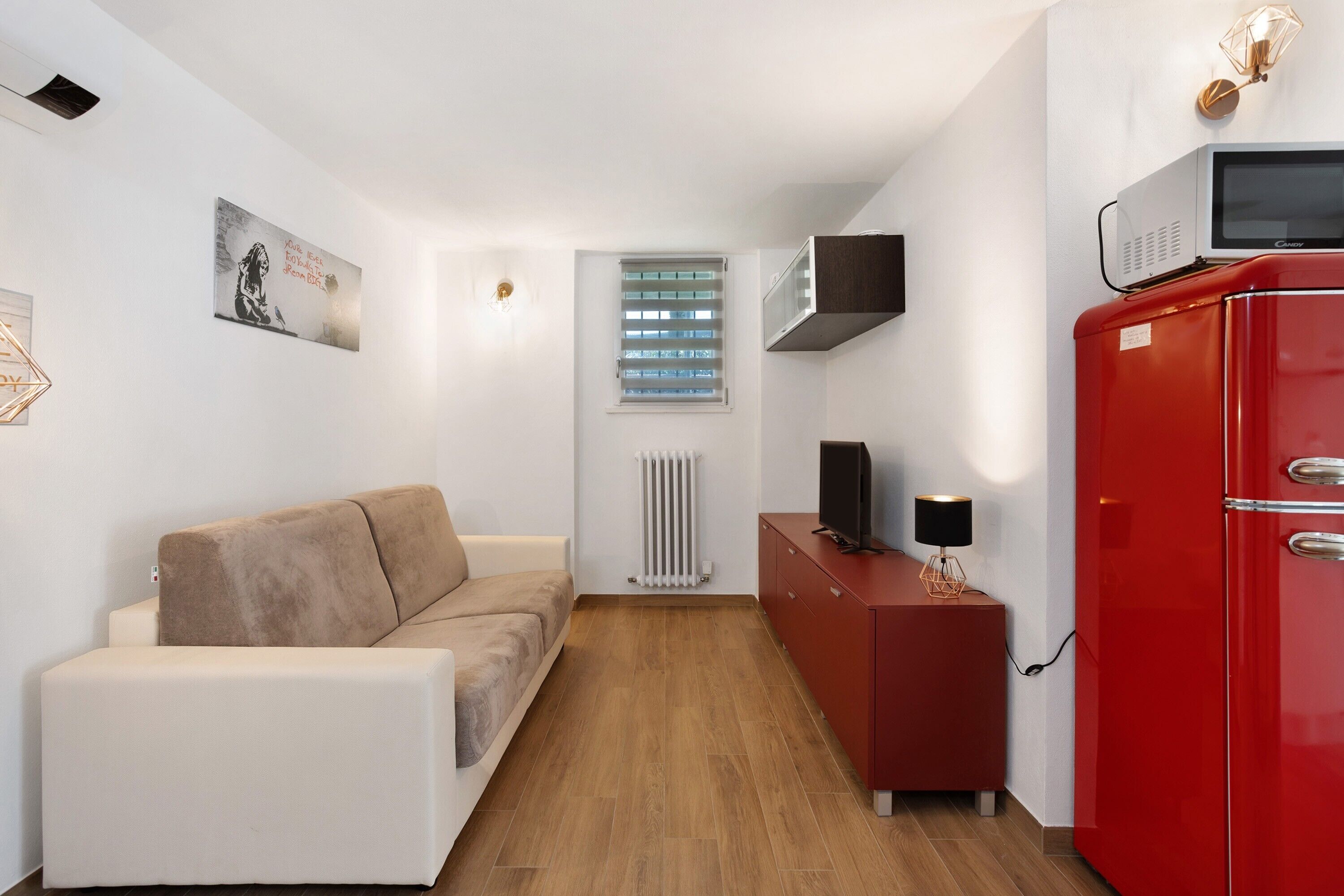 A compact living space with a sofa, a red cabinet, a television, and a radiator.