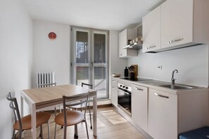Une cuisine moderne avec un coin repas, des meubles blancs, un four encastré et une fenêtre.