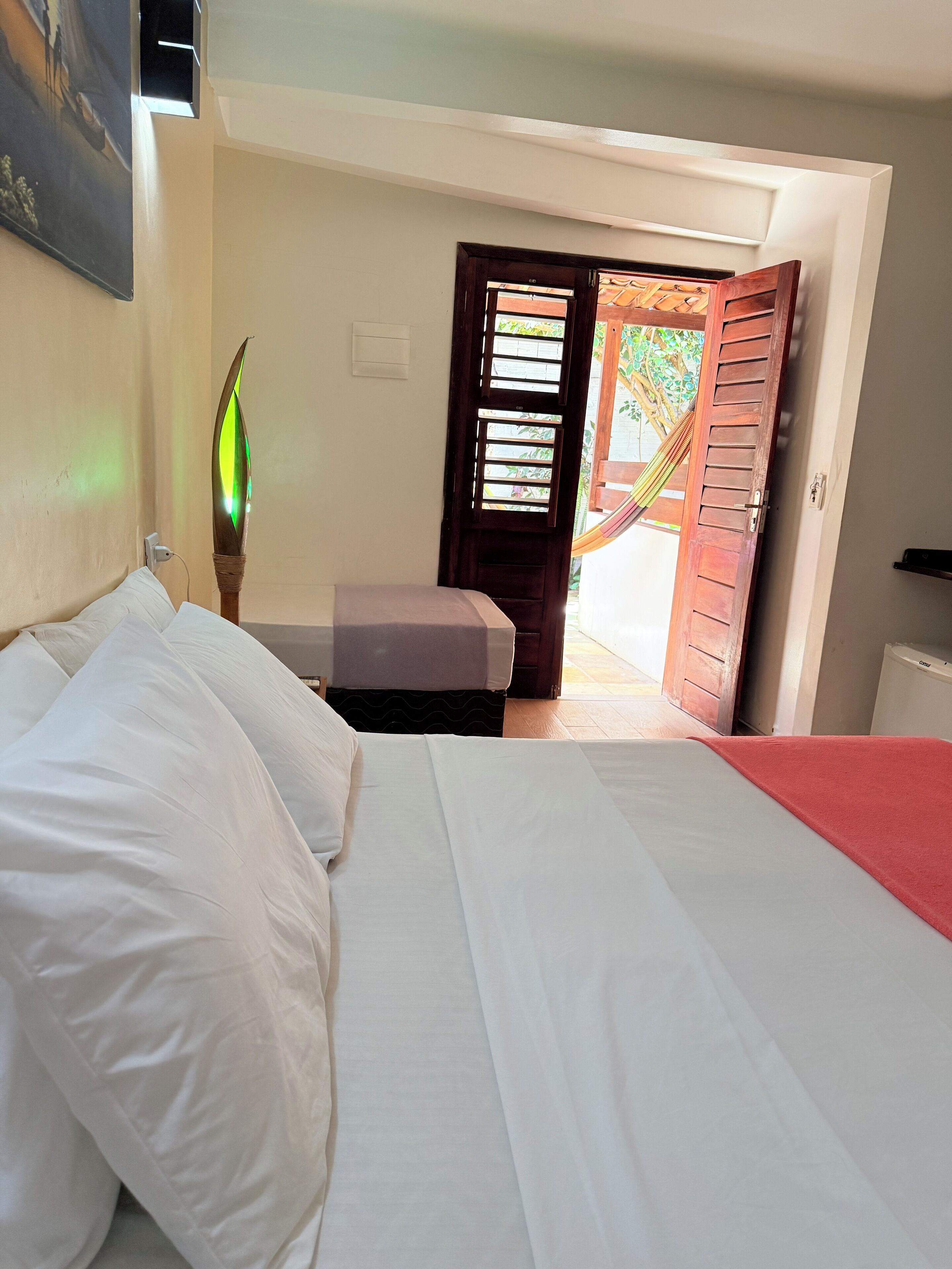 A bedroom with a bed, a bedside table, and a door leading to an outdoor area.