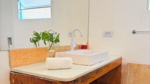 Un baño con tocador de madera, un lavabo blanco, un espejo, una ventana y un perchero para toallas.