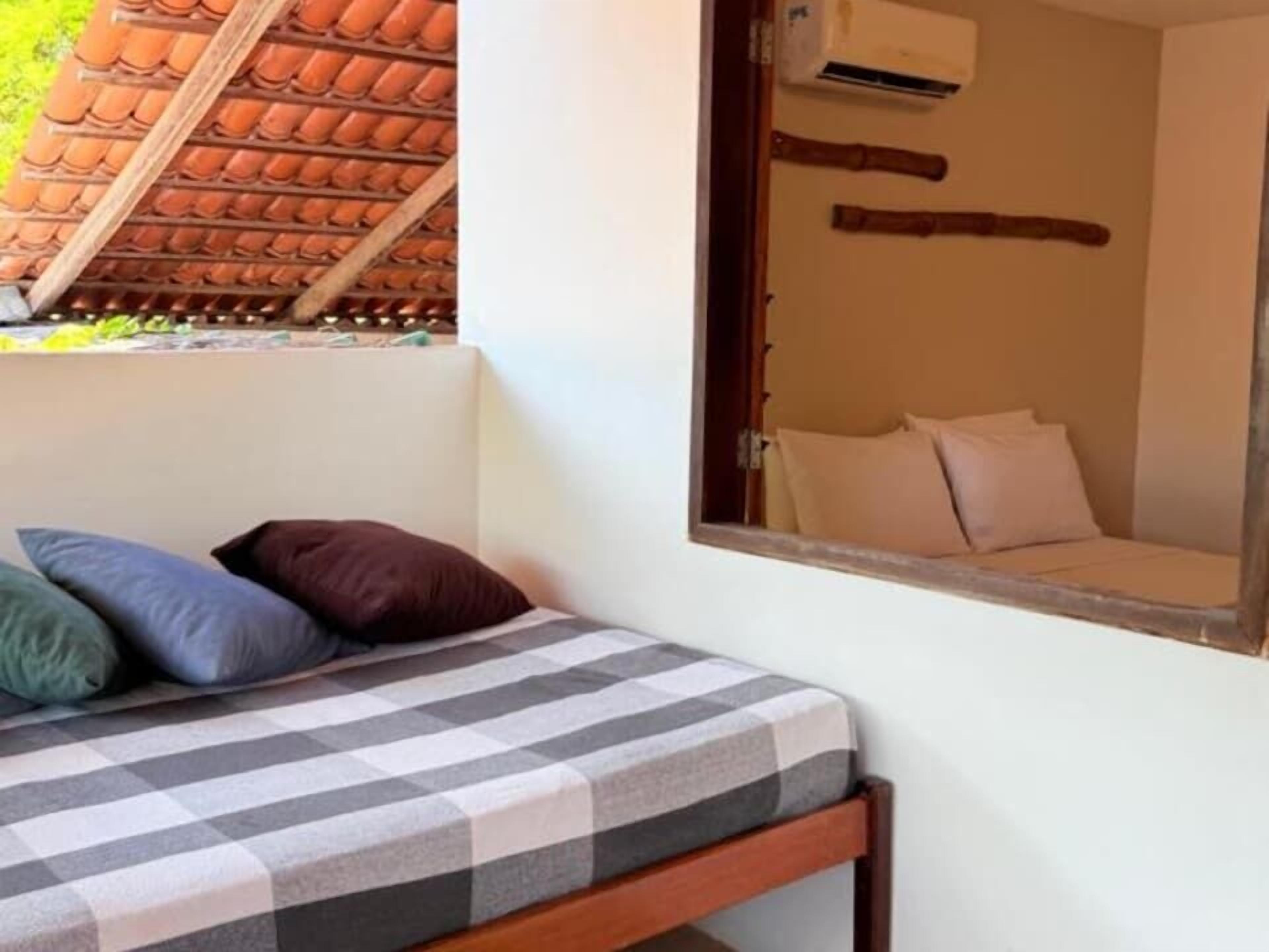 A bed with a checkered bedspread and pillows, a wooden headboard, and a window with a view of a tiled roof.