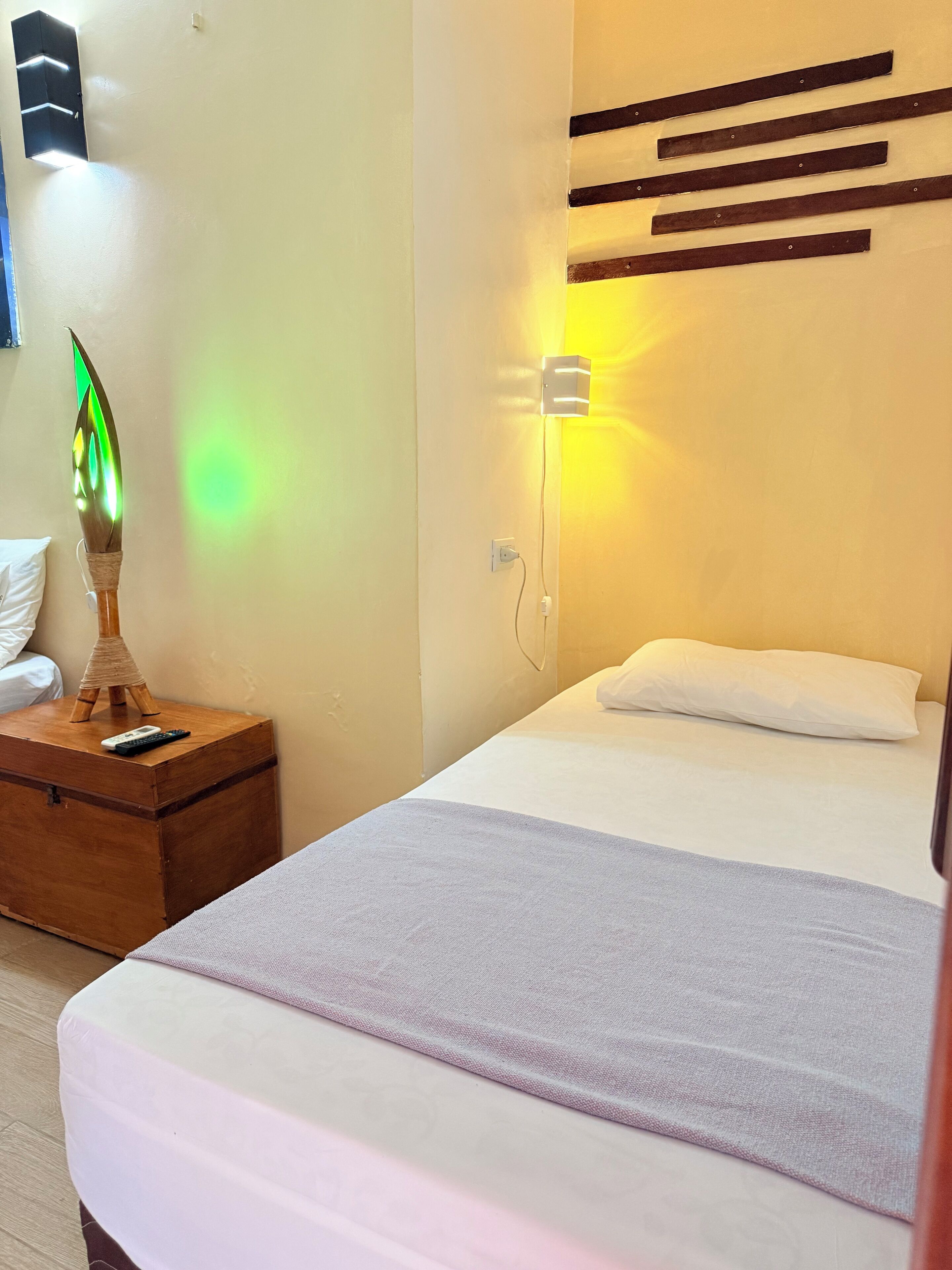 A bedroom with a bed, a nightstand with a lamp, and a wall-mounted light fixture.