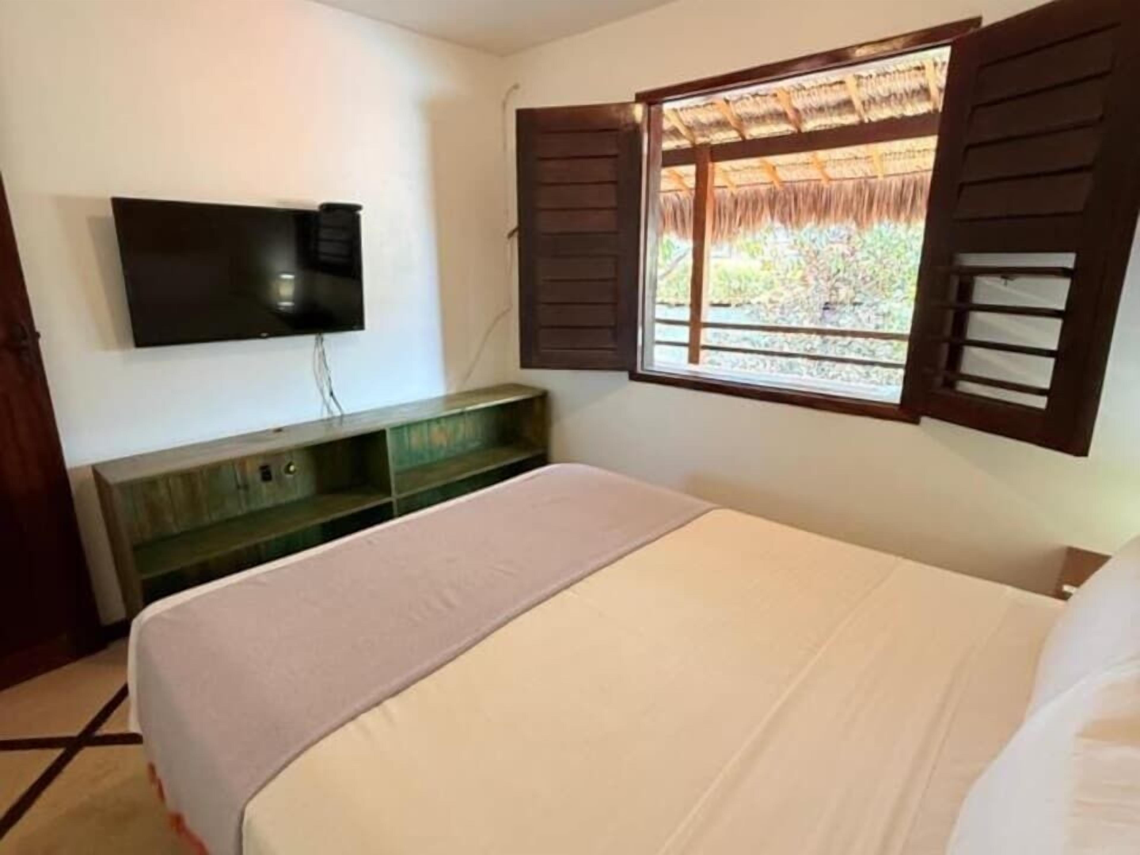 A bedroom with a bed, a television mounted on the wall, and a window with shutters.