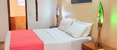 A bedroom with a bed, bedside table, lamp, and a painting on the wall.