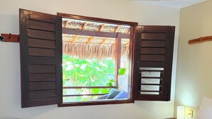 Un dormitorio con cama, mesita de noche, ventana con contraventanas de madera y vista a espacios verdes.