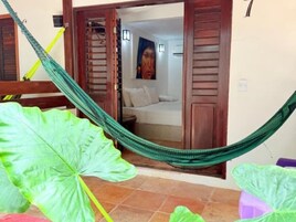 A room with a hammock, a bed with white bedding, and a large green plant.