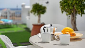 A round table with two white mugs, a coffee pot, and a plate with lemons. There are two potted plants on the table.