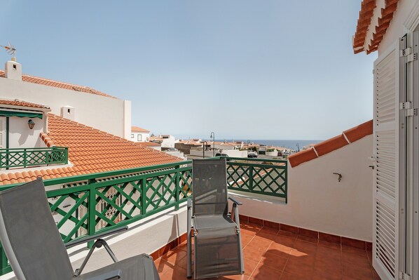A balcony with a green lattice railing, a chair, and a view of the sea.