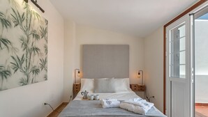 Ein Hotelzimmer mit einem Bett, Nachttischen, einem Gemälde und Blick durch eine Tür.