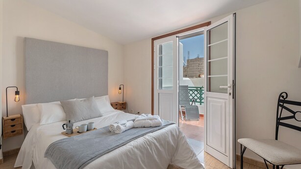 Ein Schlafzimmer mit Bett, Nachttischen, einem Sessel, einer Balkontür und Blick ins Freie.