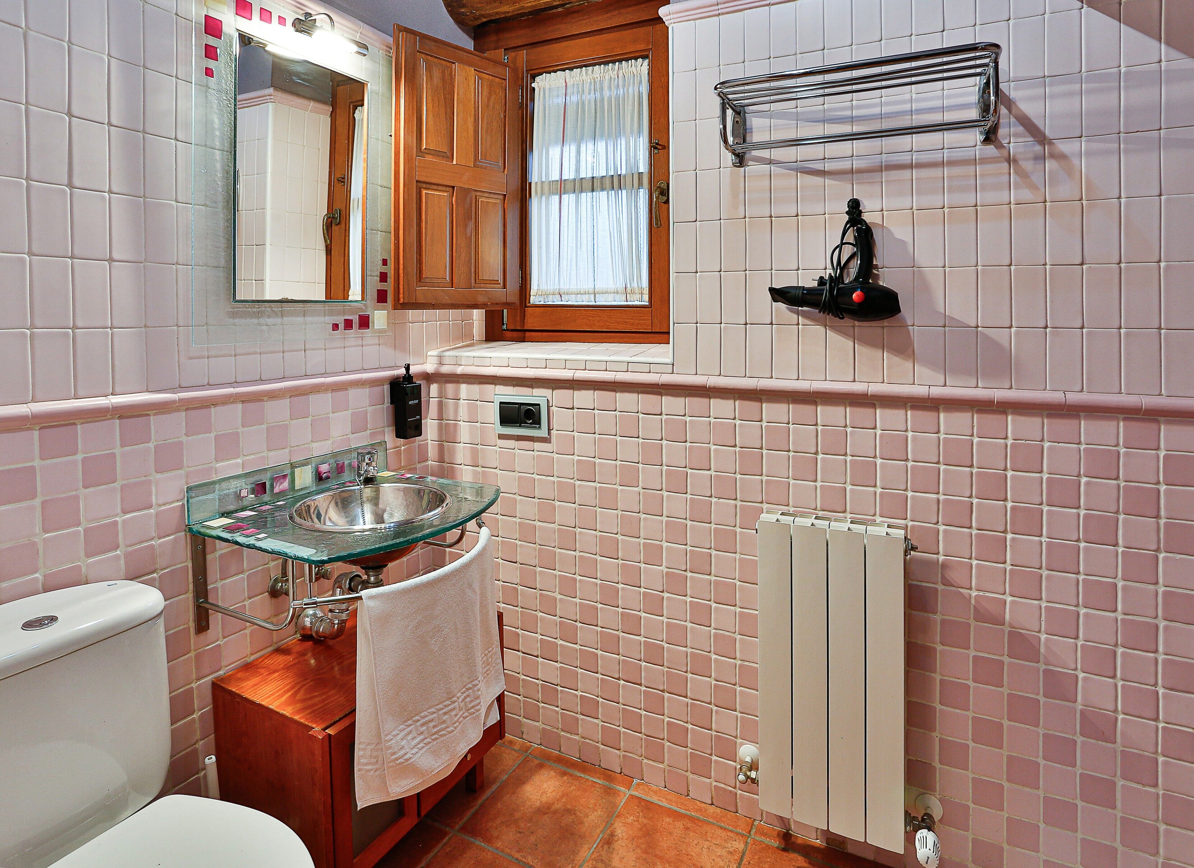 Un baño con lavamanos de vidrio, gabinete de madera y un perchero para toallas.