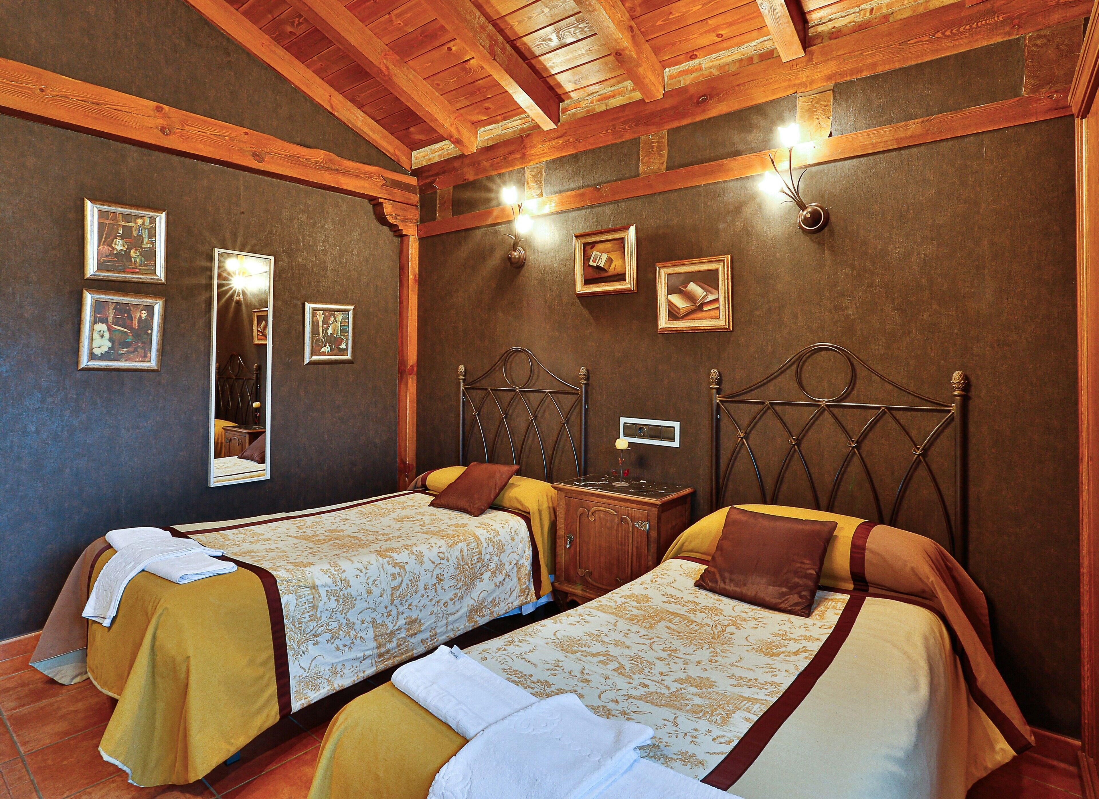 Een kamer met twee bedden, houten balken in het plafond en ingekaderde foto's aan de wanden.