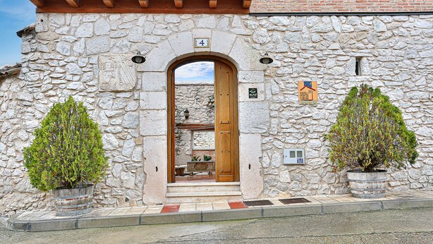 Ein Steinhaus mit einer Holztür, einer Glocke und zwei Blumentöpfen.
