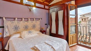 Ein Schlafzimmer mit Bett, Holz-Kopfteil, Nachttisch, einer Blumenvase und einem Balkon mit Blick auf Gebäude.