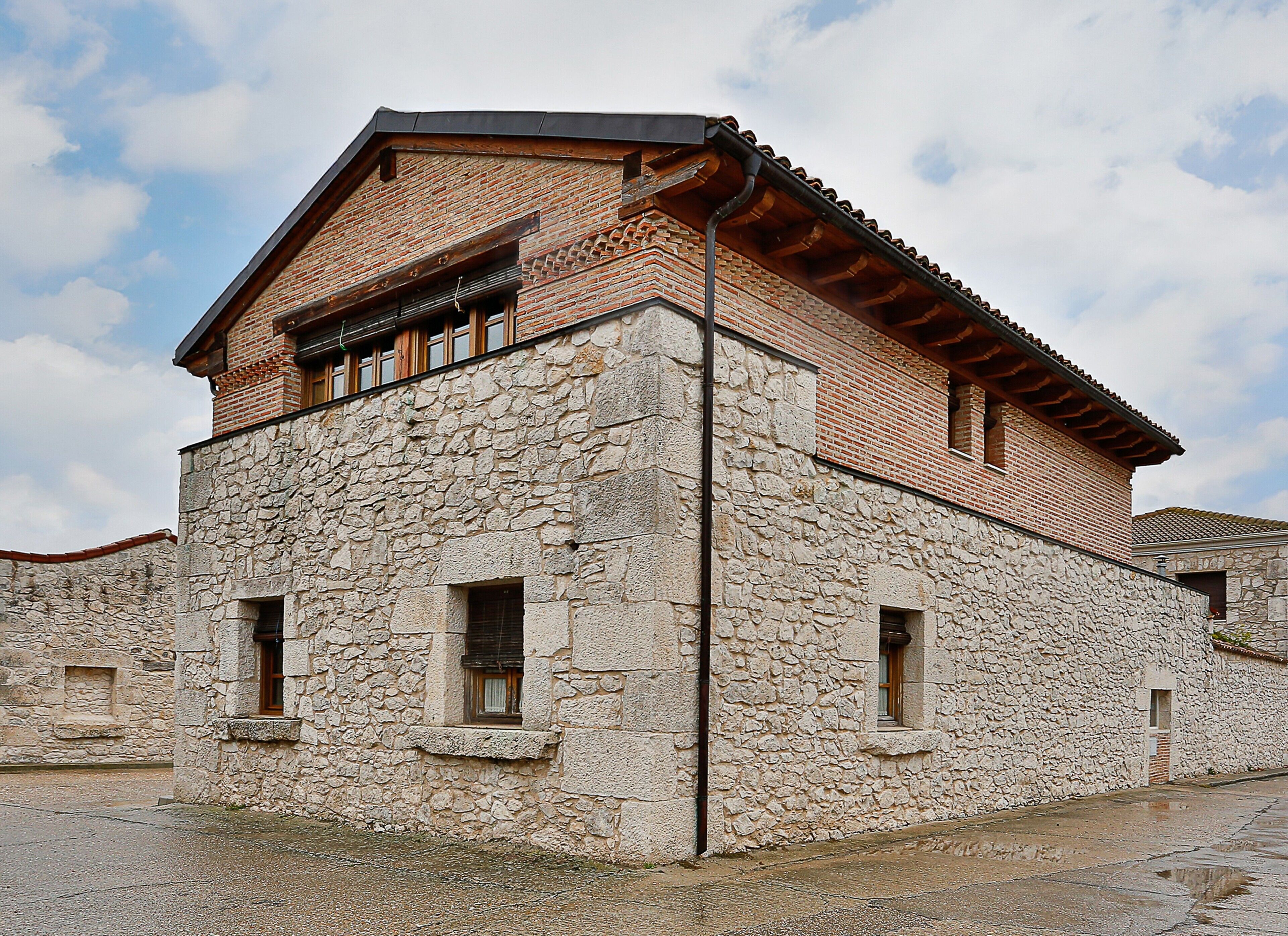 A stone building with a brick upper section, multiple windows, and a tiled roof.