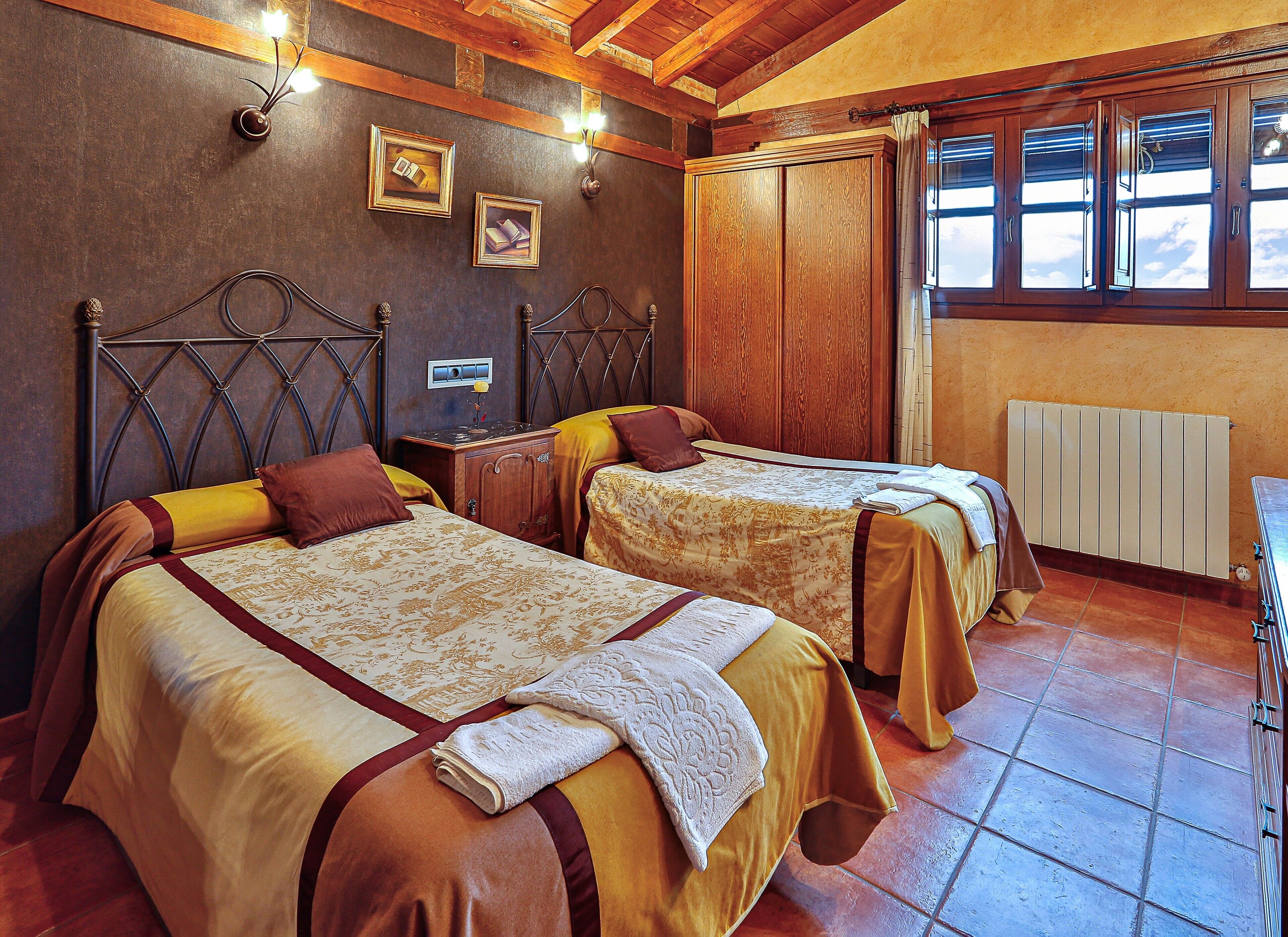 A hotel room with two beds, wooden headboards, a radiator, and a window with curtains.