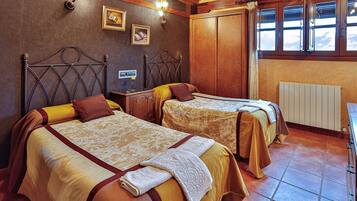 A hotel room with two beds, wooden headboards, a radiator, and a window with curtains.