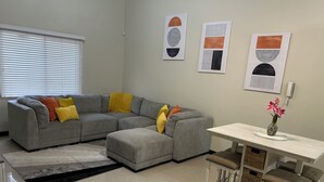 A living room with a grey sectional sofa, a small white table, and a vase with flowers. - Charming 2-bedroom apartment with WiFi, AC in wonderful Kingston (Kingston)