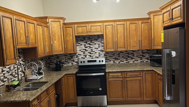 A kitchen with wooden cabinets, a stainless steel refrigerator, a black oven, and a tiled backsplash. - Charming 2-bedroom apartment with WiFi, AC in wonderful Kingston (Kingston)