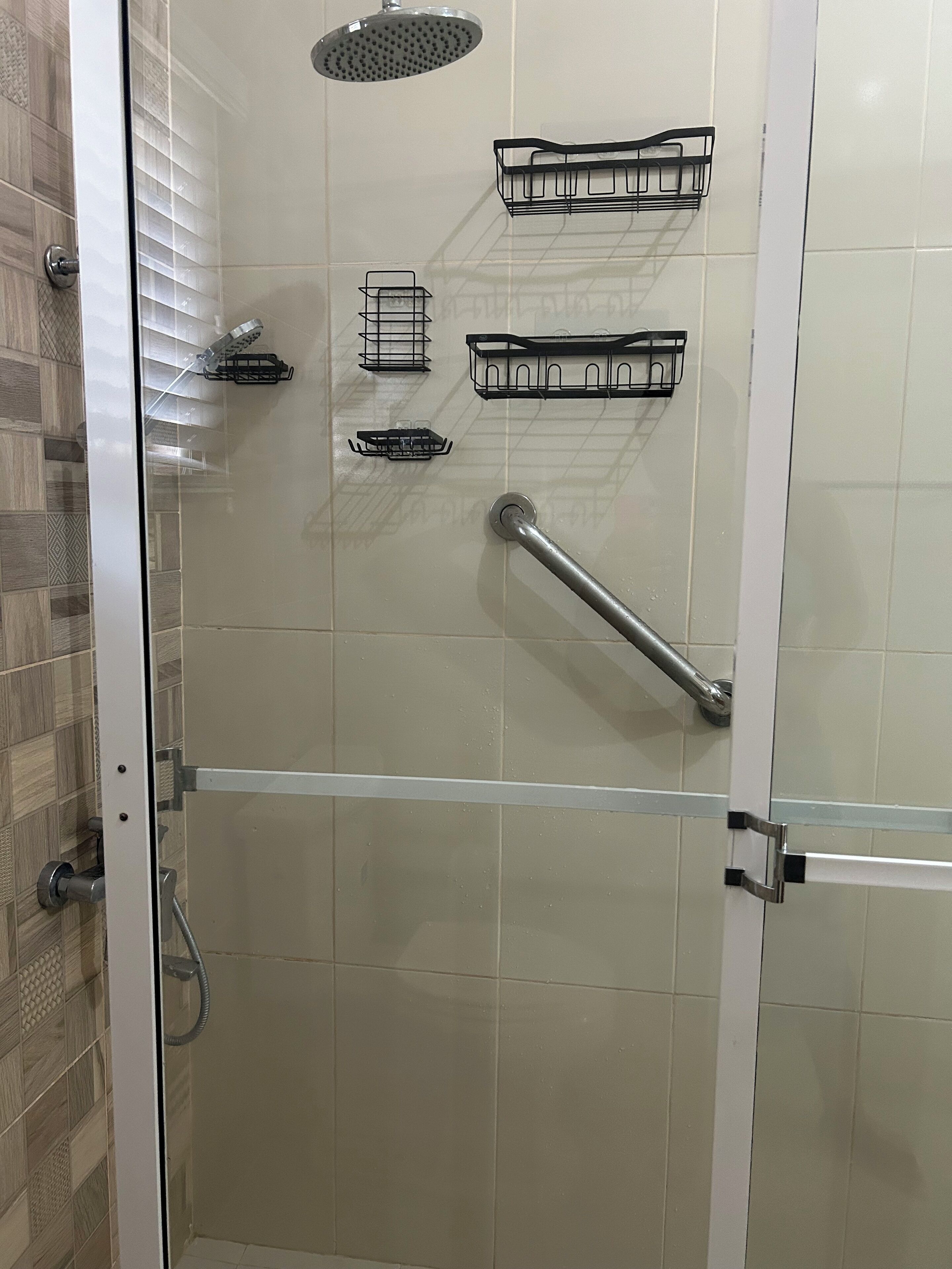 A shower area with a glass door, a handheld showerhead, a handheld shower attachment, and a grab bar.