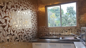 Eine Küche mit geometrischer Spritzschutzleiste, einem Fenster mit Blick ins Grüne und einer Spüle aus Edelstahl.