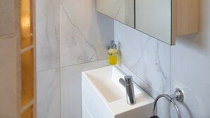 Ein Badezimmer mit einem weißen Waschbecken, einem Spiegel und Marmorfliesen.