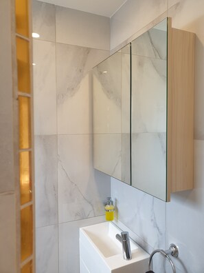 Features a sleek vanity with a large mirror and marble tiles.