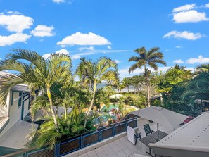 A rooftop terrace with a pool, palm trees, and a view of the ocean.