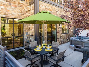 Eine Terrasse im Freien mit Tisch, Stühlen und einem grünen Sonnenschirm.